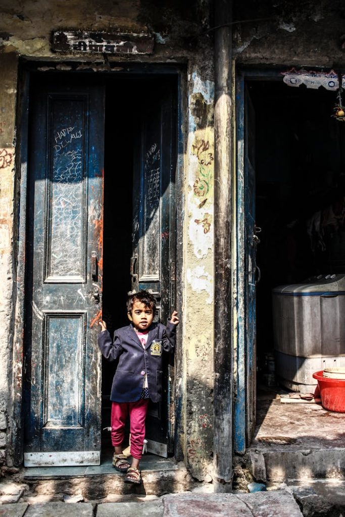 A young child stands in a doorway, capturing innocence in an urban Indian street scene.